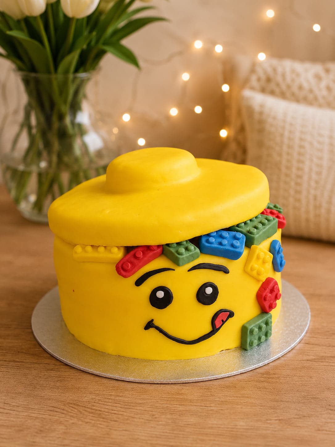 Fondanttaart in de vorm van een LEGO-hoofd met gele helm en gekleurde blokjes